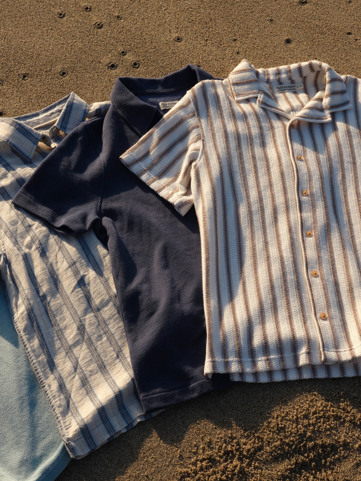 Two shirts, one dark and one striped, on a sandy surface