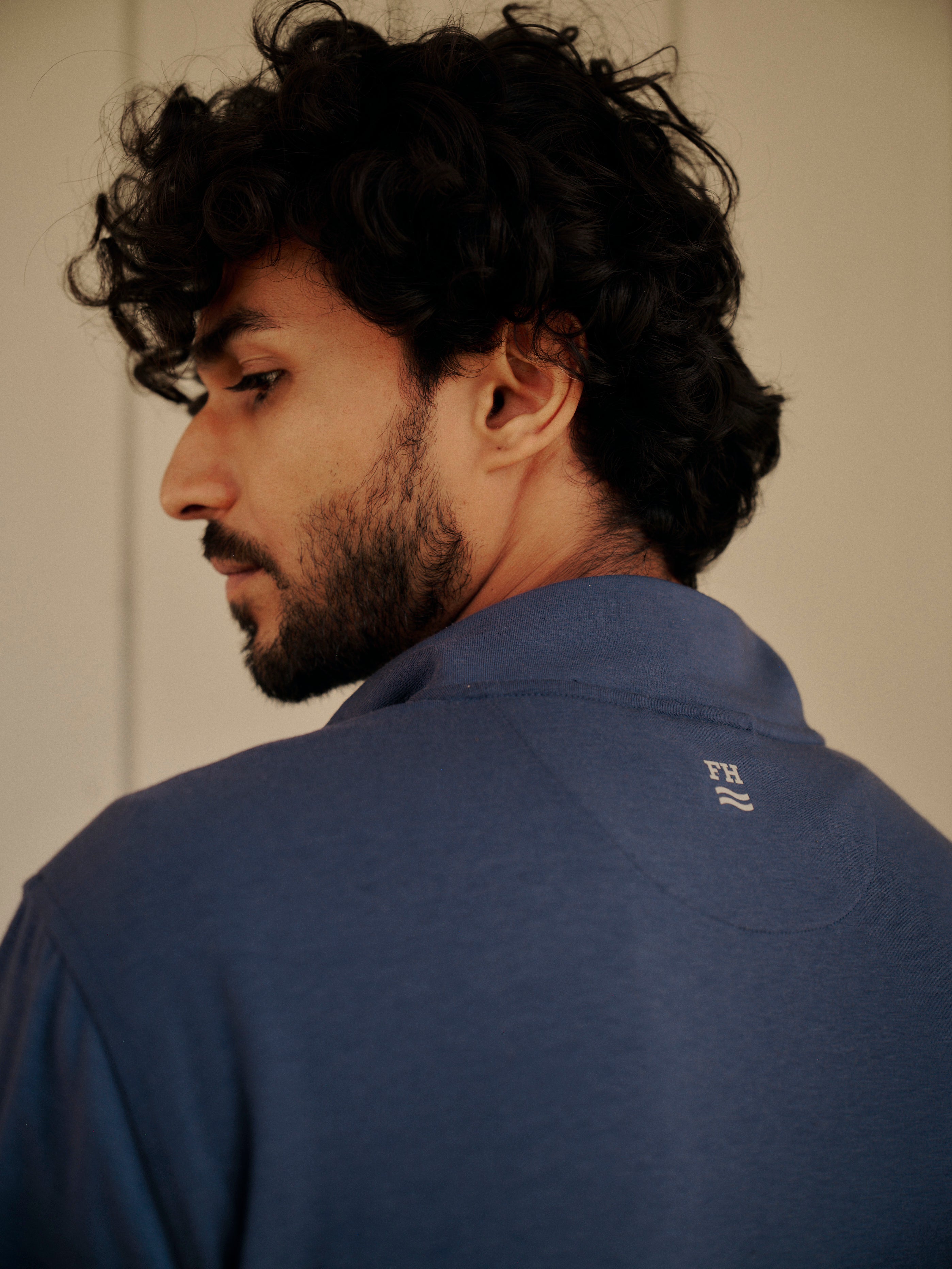 Man wearing a navy blue compass quarter zip with a visible brand logo, looking over his shoulder.