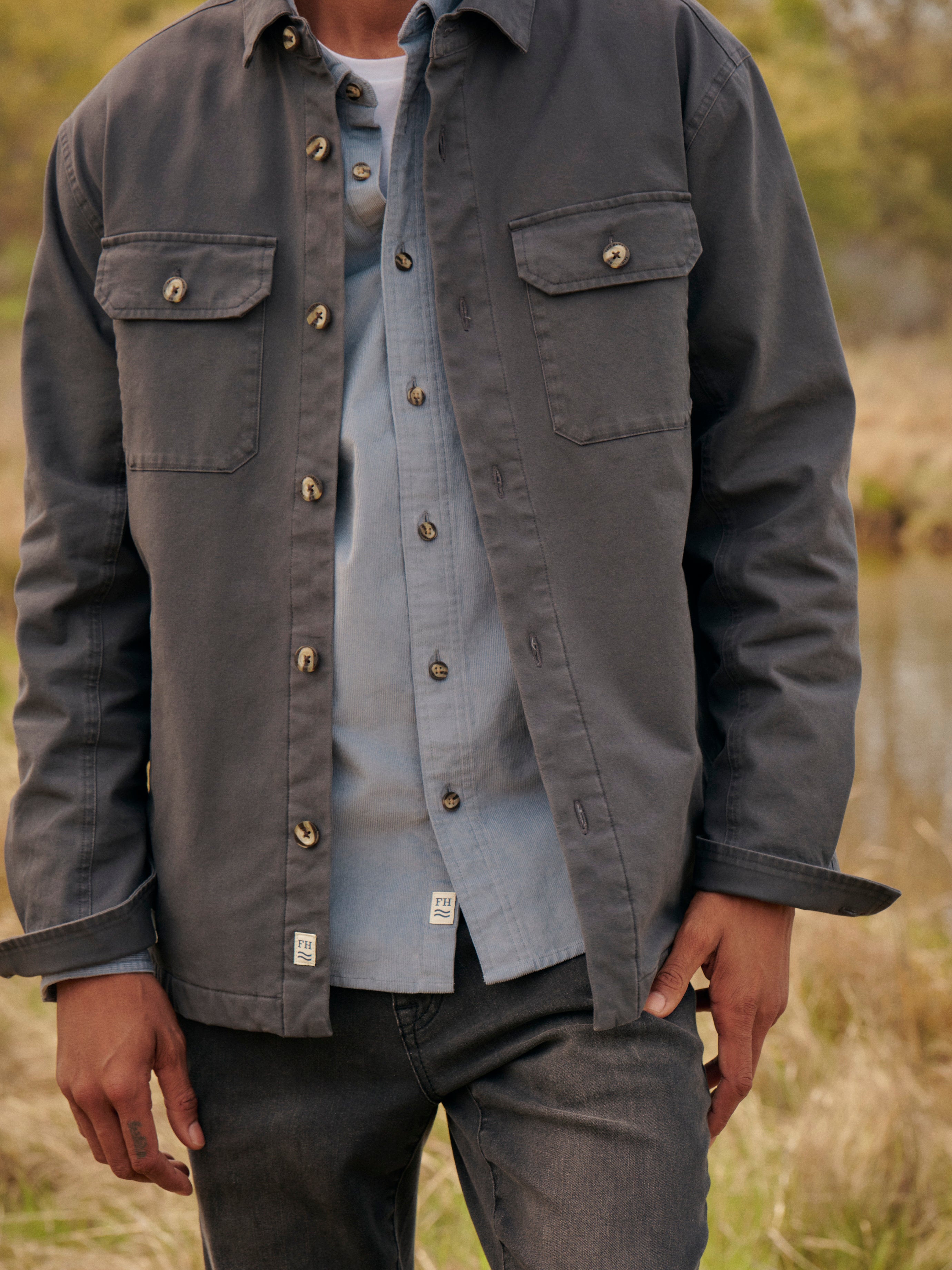 Person wearing a black Montauk jacket over a blue wilder corduroy shirt in an outdoor setting. 
