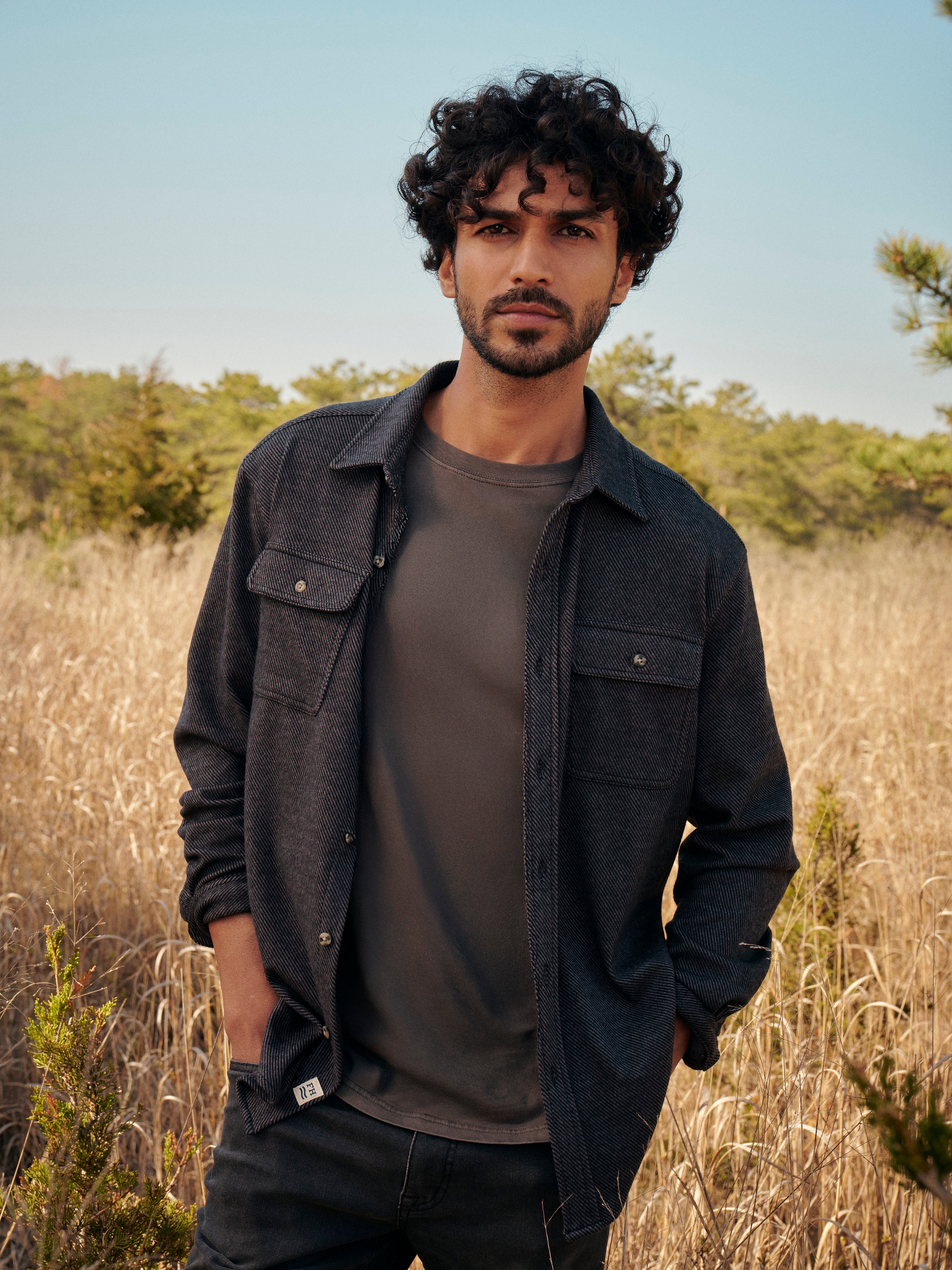 Man wearing a black dunewood twill flannel  over a black saltaire t-shirt in a natural setting with trees and clear sky.