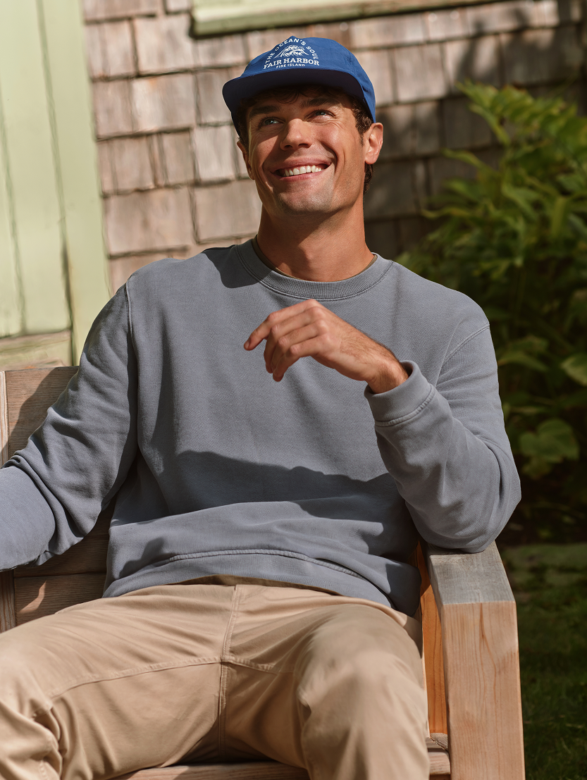 Man wearing a blue cap and gray sweatshirt sitting outdoors.
