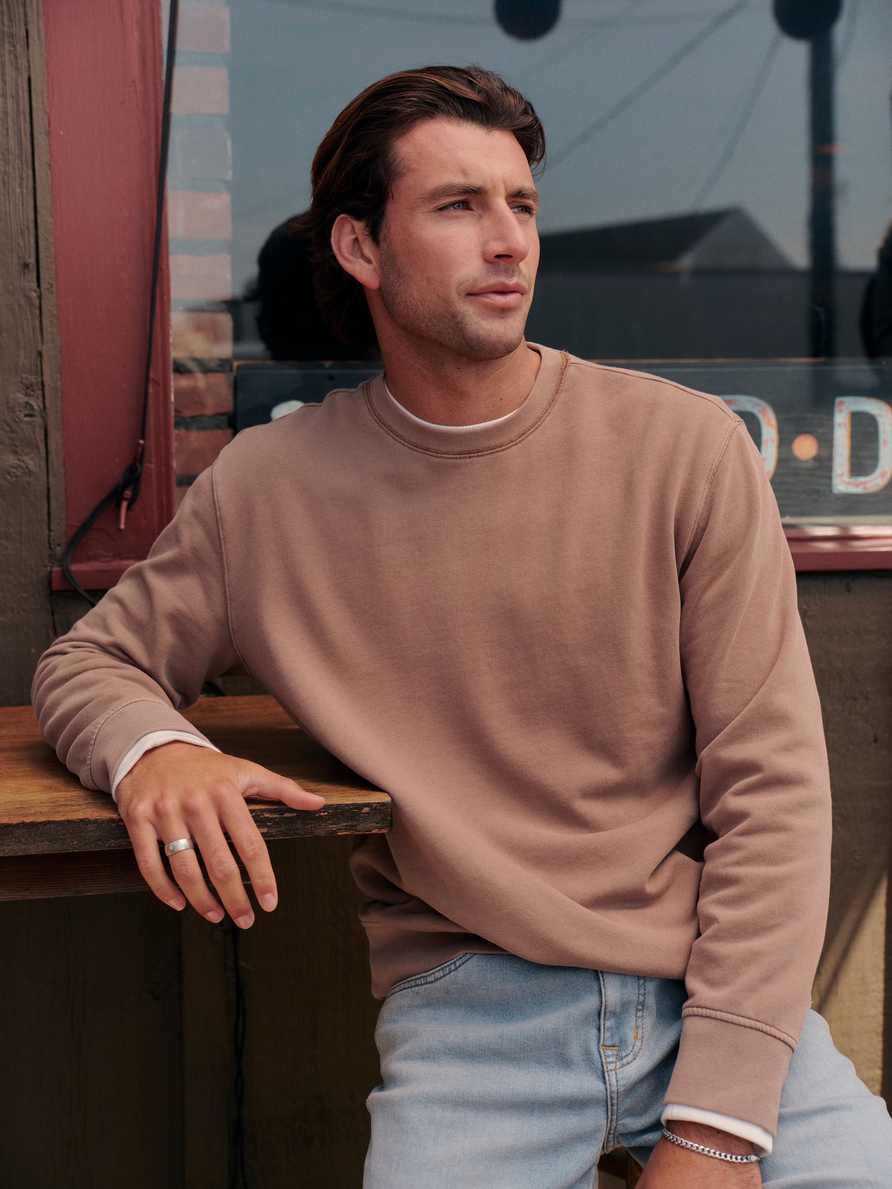 Man wearing a oak saltaire sweatshirt and light blue jeans sitting on a bench.