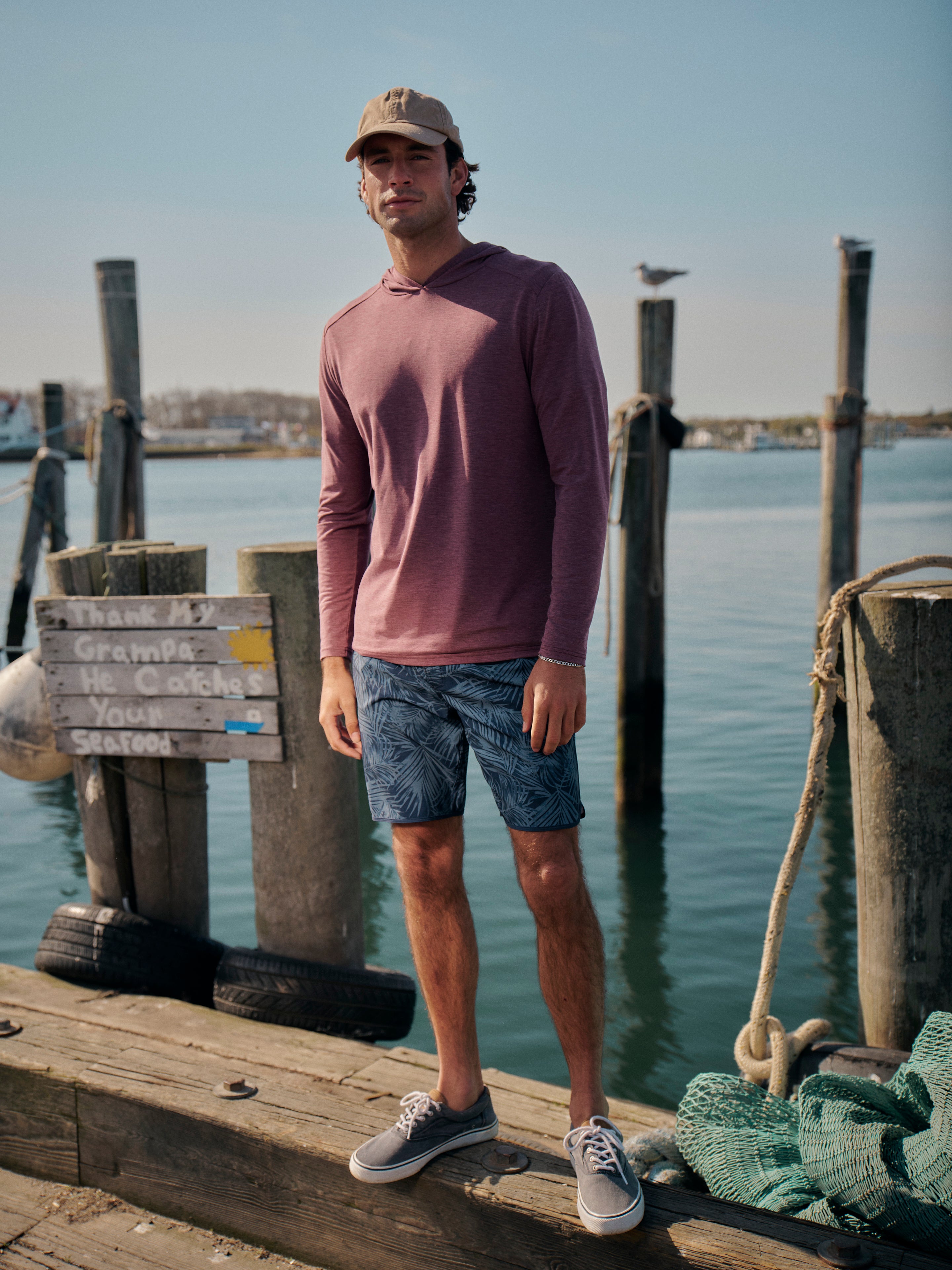 Man standing on a dock by water wearing a red seabreeze hoodie  and anchor trunk in grey floral colorway.