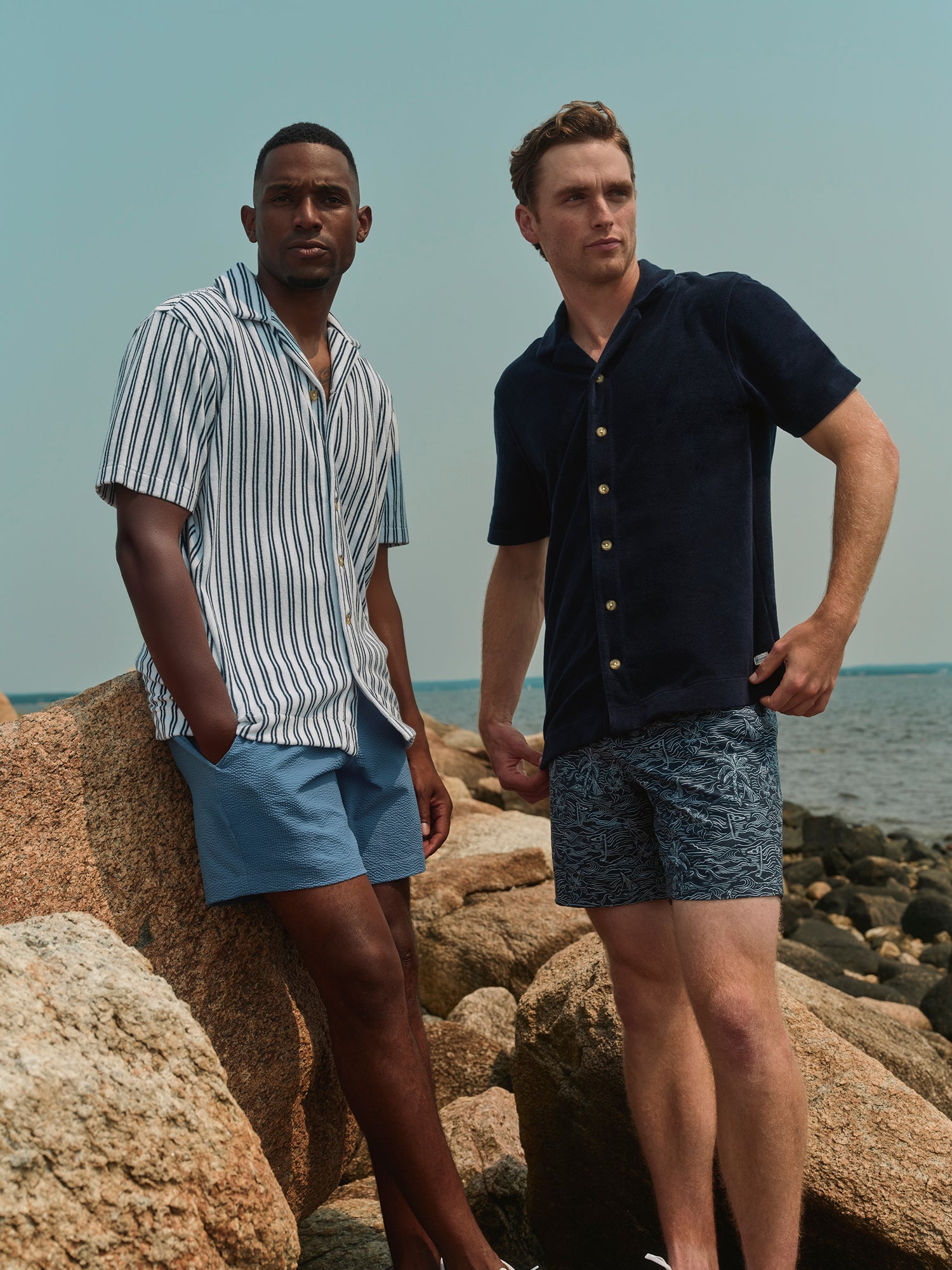 Two men standing on rocky beach with ocean in the background