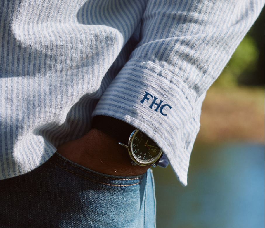 Close-up of a person wearing a light blue corduroy shirt with 'FHC' monogrammed on the sleeve, outdoors. Promoting custom embroidery 