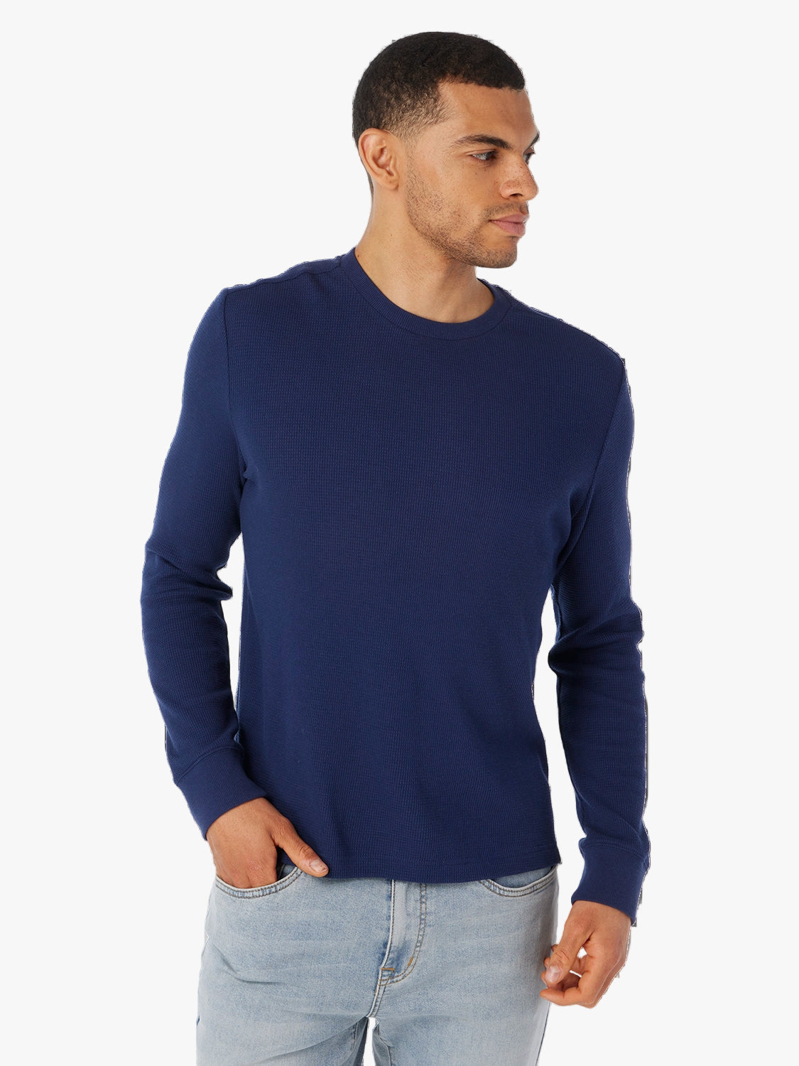 Man wearing a navy long-sleeve waffle fabric shirt and light blue jeans on a white background