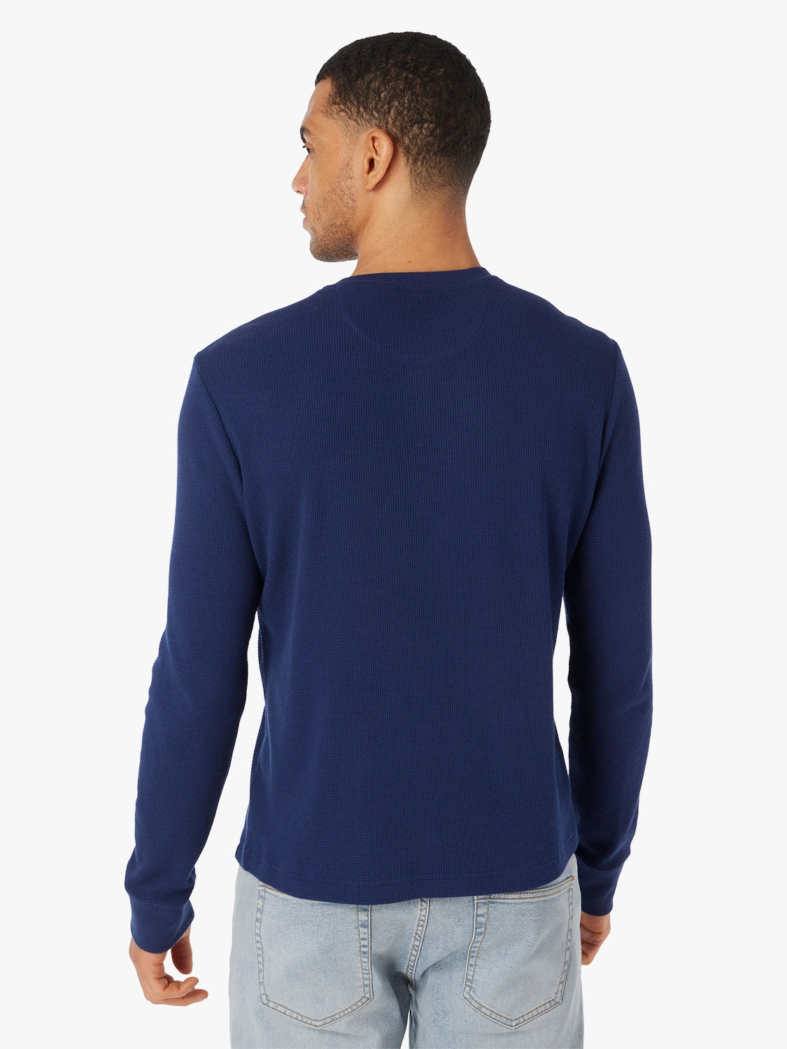 Man wearing a navy long-sleeve waffle fabric shirt and light blue jeans on a white background, showing the back view. 