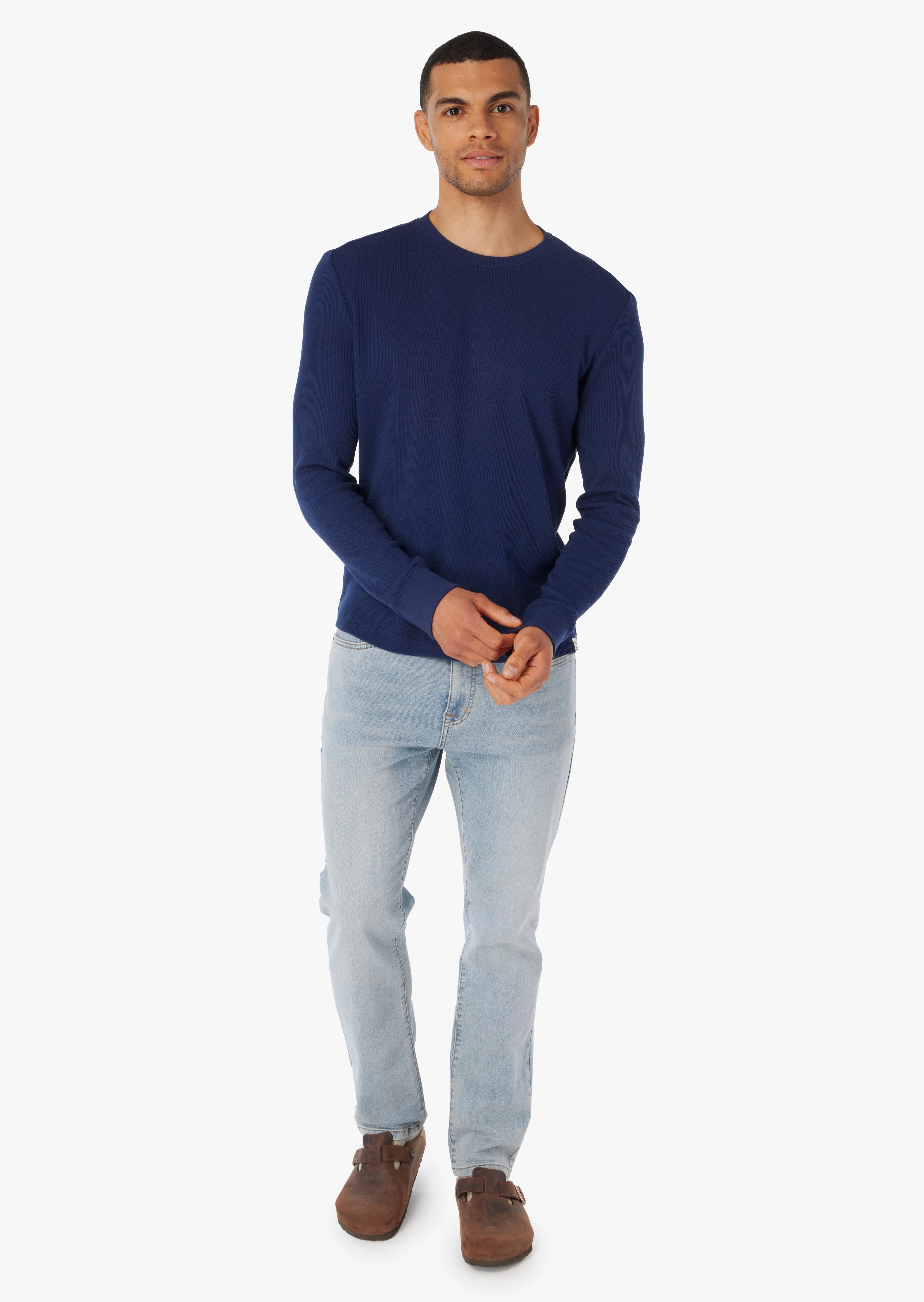 Man wearing a navy waffle fabric shirt  and light blue jeans on a white background