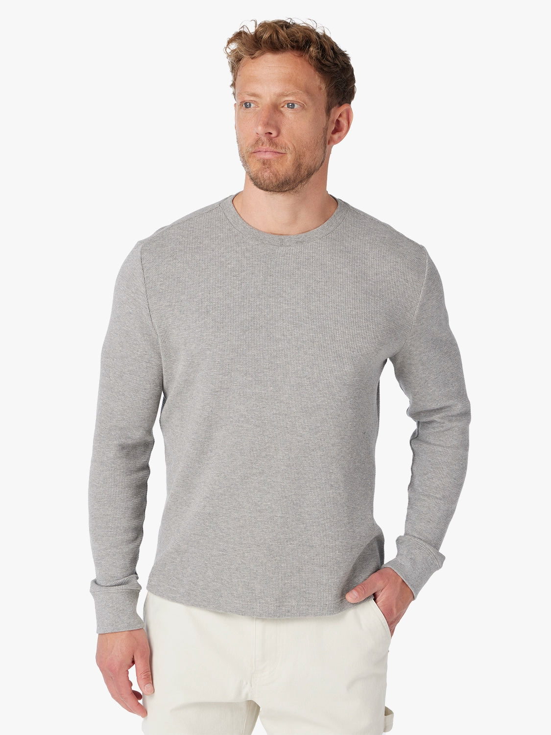 Man wearing a gray waffle long sleeve shirt and white pants on a white background