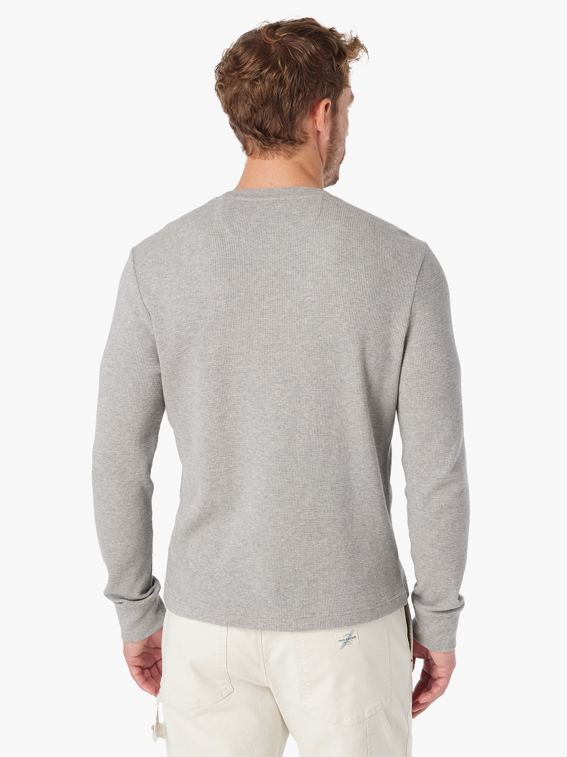 Man wearing a gray waffle long sleeve shirt and white pants on a white background, showing the back view. 