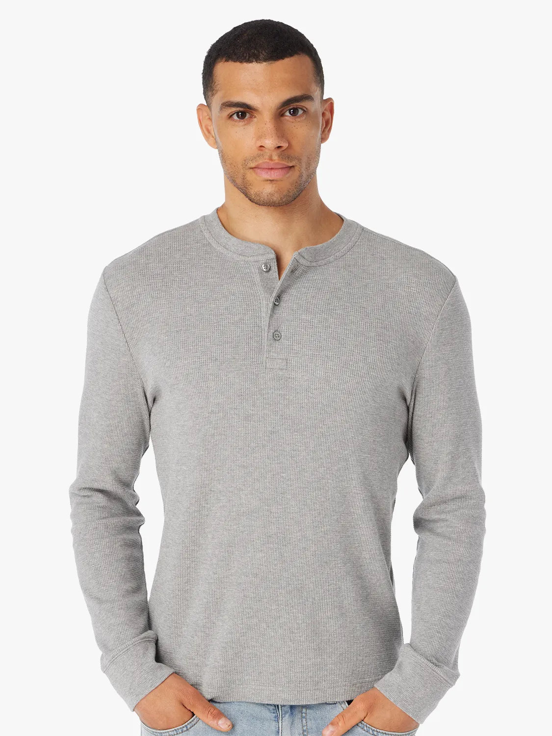 Man wearing a gray long-sleeve waffle henley shirt on a white background, paired with jeans. 