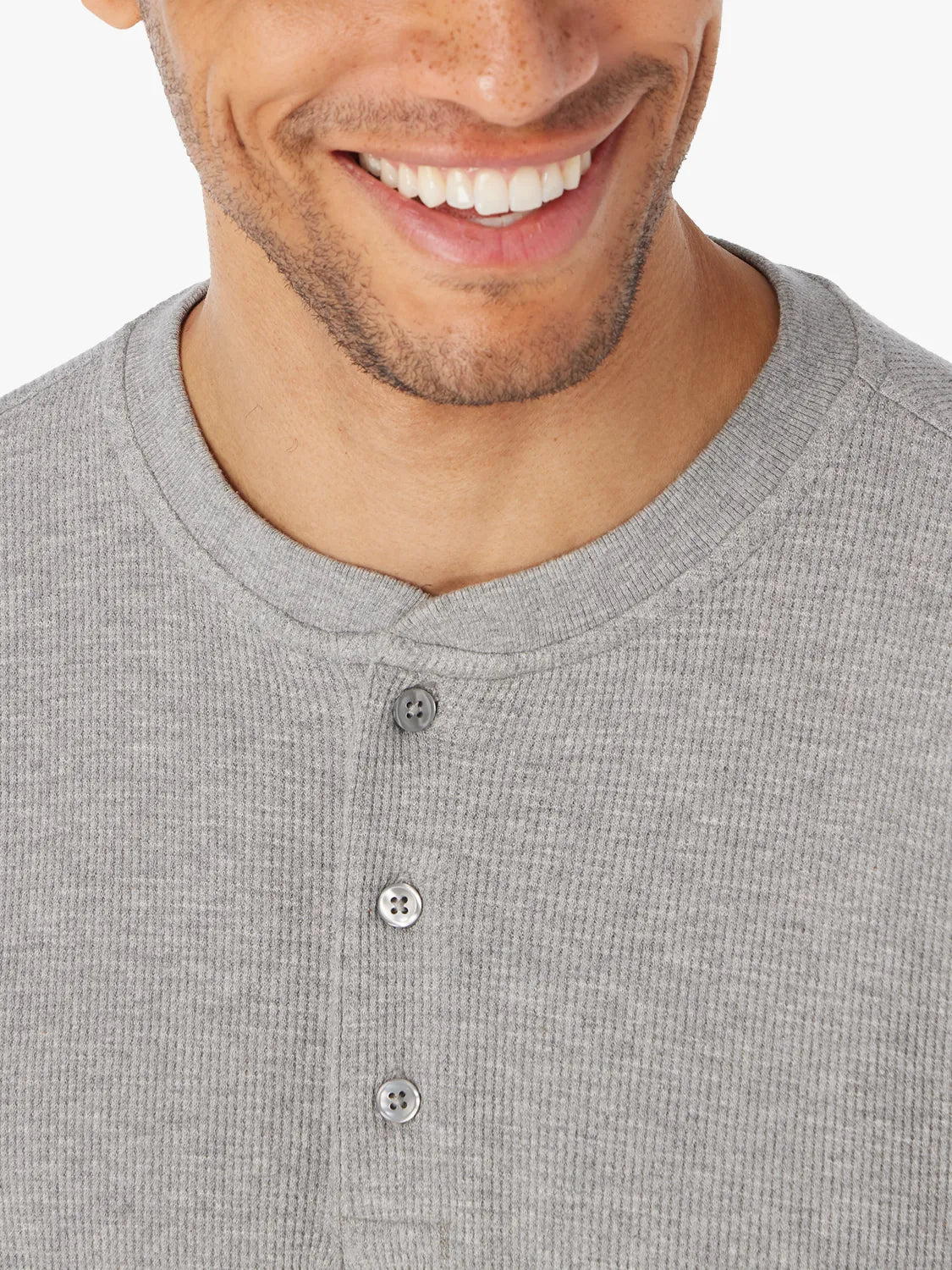 Close-up of a person wearing a gray waffle henley fabric and button-up detail of shirt with a white background