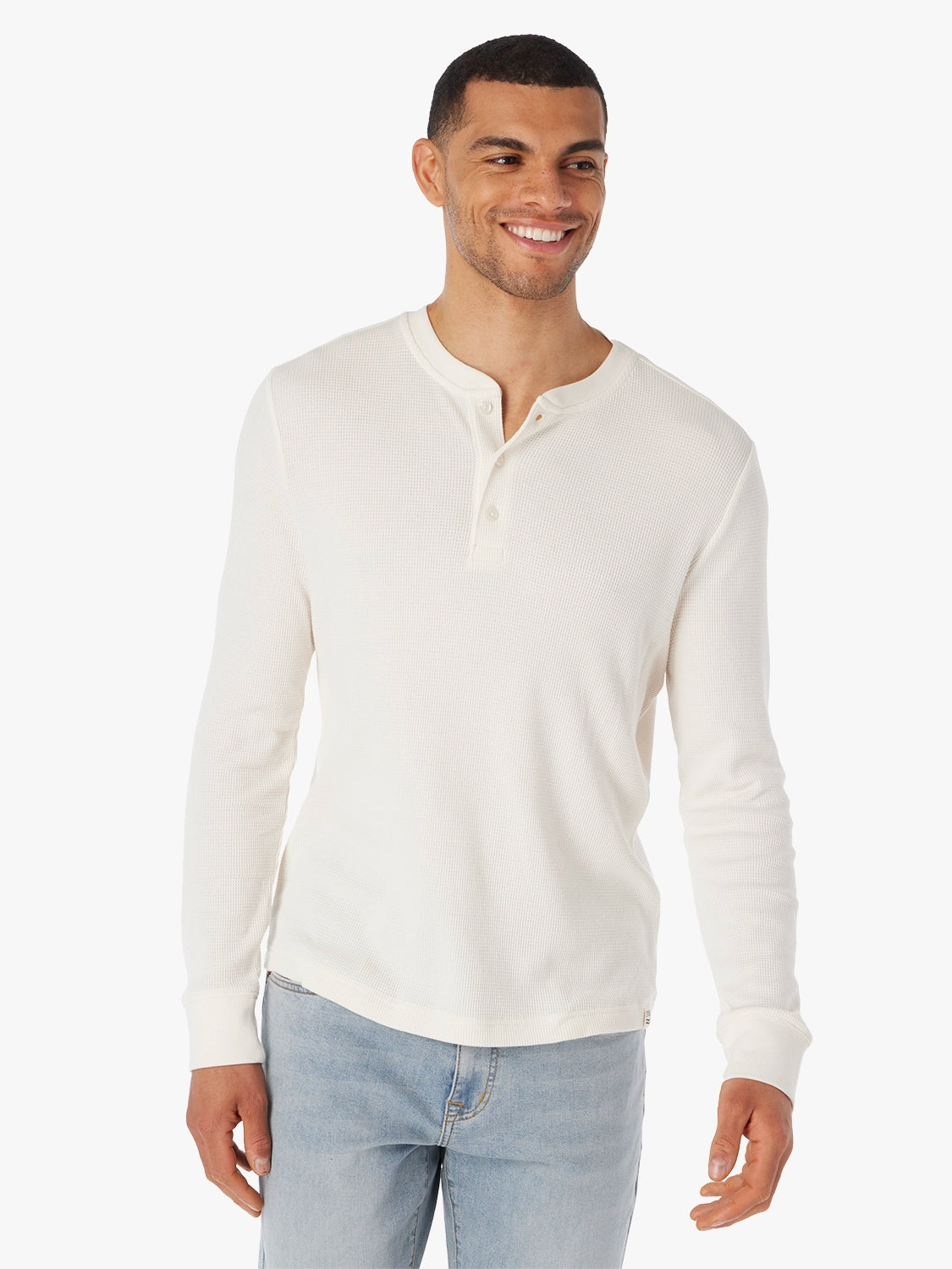 Man wearing a cream long-sleeve waffle fabric henley shirt and light blue jeans on a white background