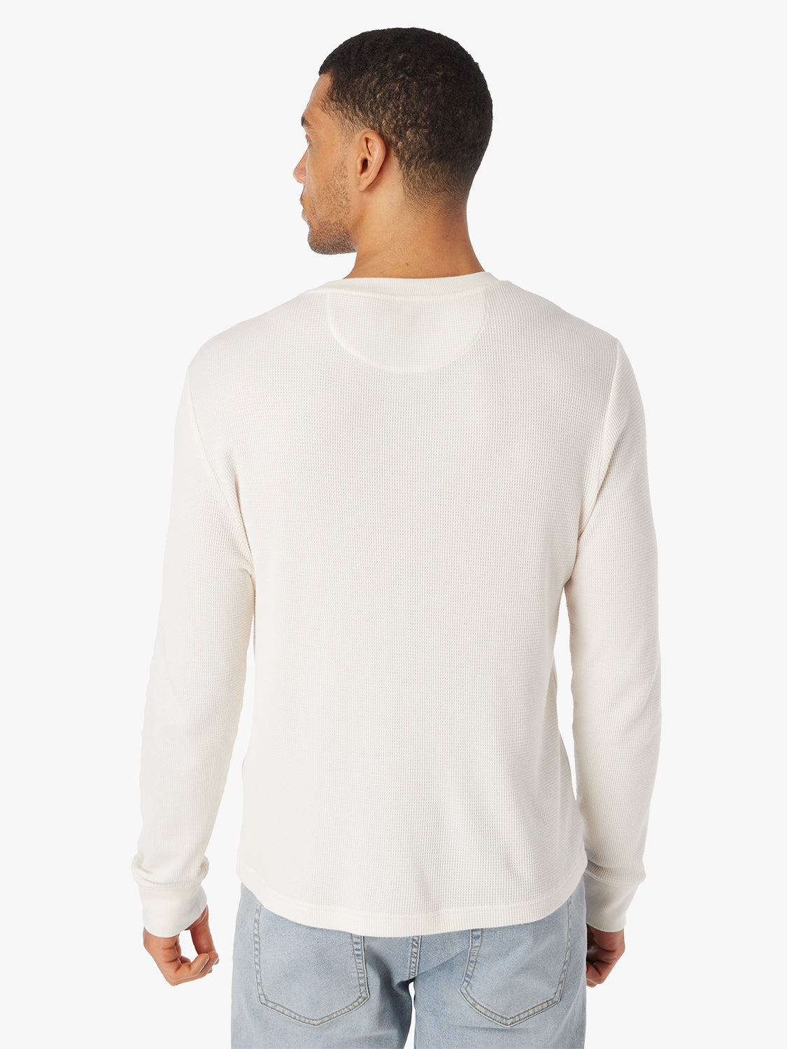 Man wearing a cream long-sleeve waffle fabric henley shirt and light blue jeans on a white background, showing the back view of shirt 