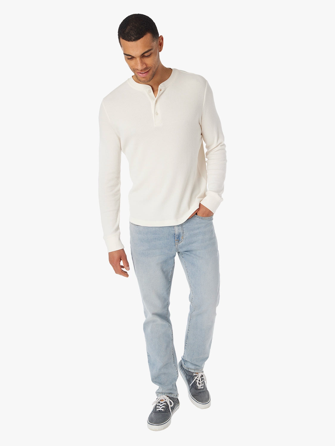 Man wearing a cream waffle long-sleeve henley shirt and light blue jeans on a white background