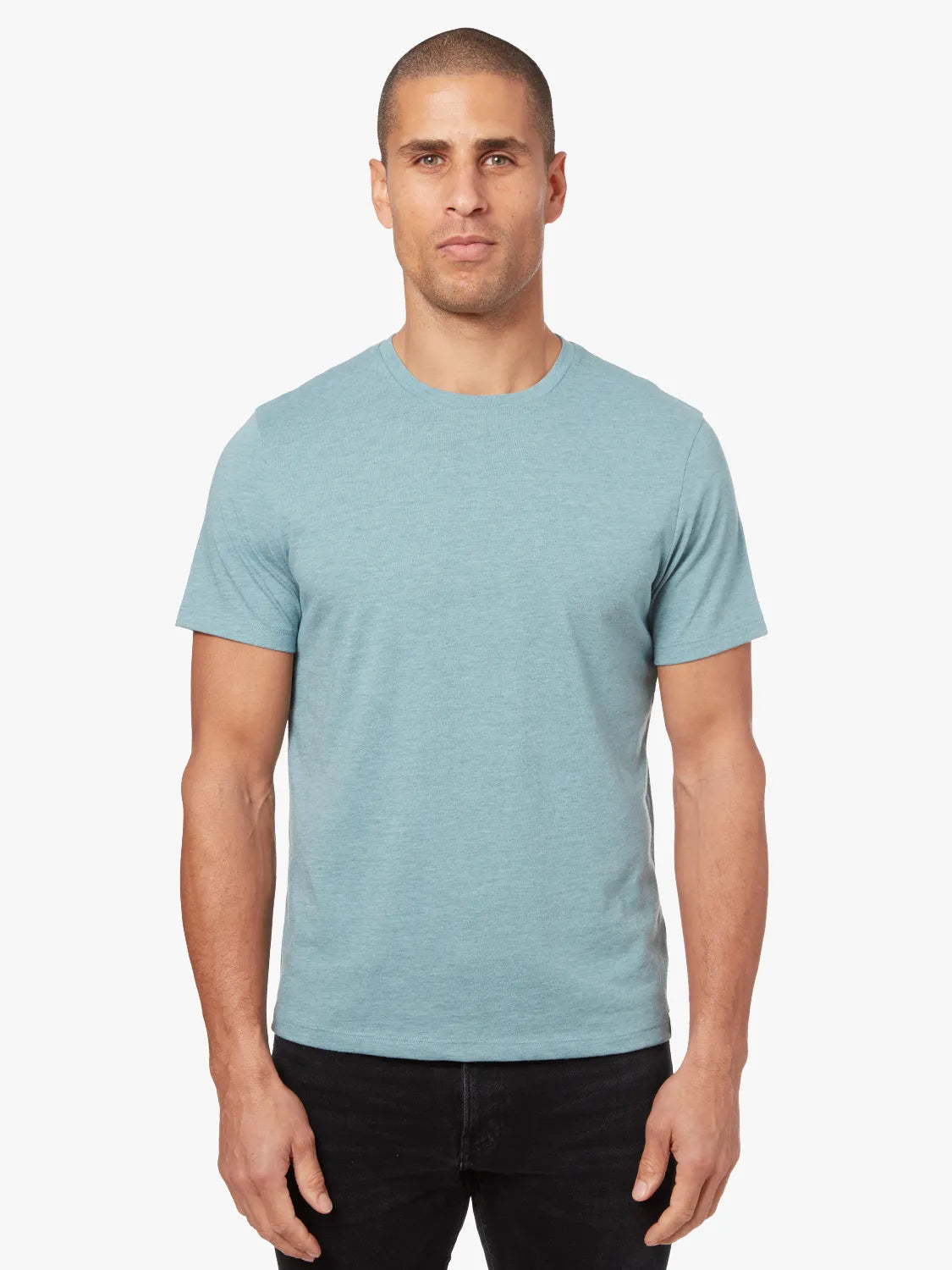 Person wearing heather light green kismet t-shirt on a white background, paired with driftwood denim pants. 
