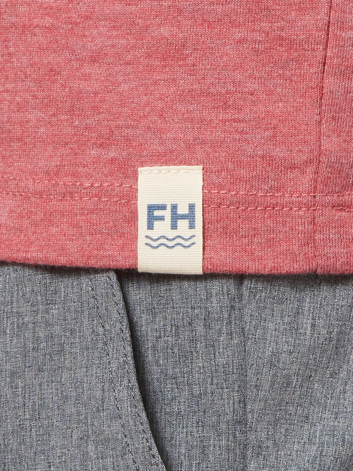 Close up of fabric for red kismet t-shirt and brand logo patch at bottom hem on, paired with grey one pants. 