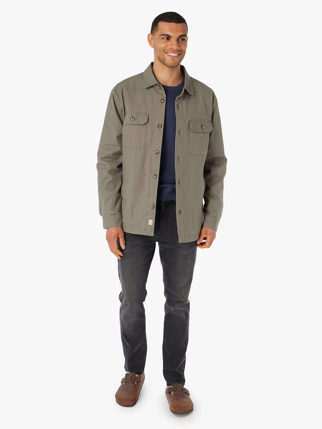 Man wearing a olive green jacket and dark jeans on a white background