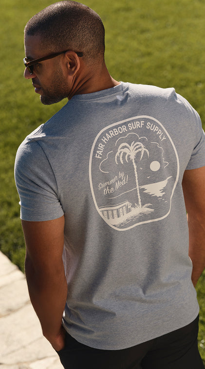 Man wearing a gray t-shirt with a beach-themed graphic on the back, standing outdoors.