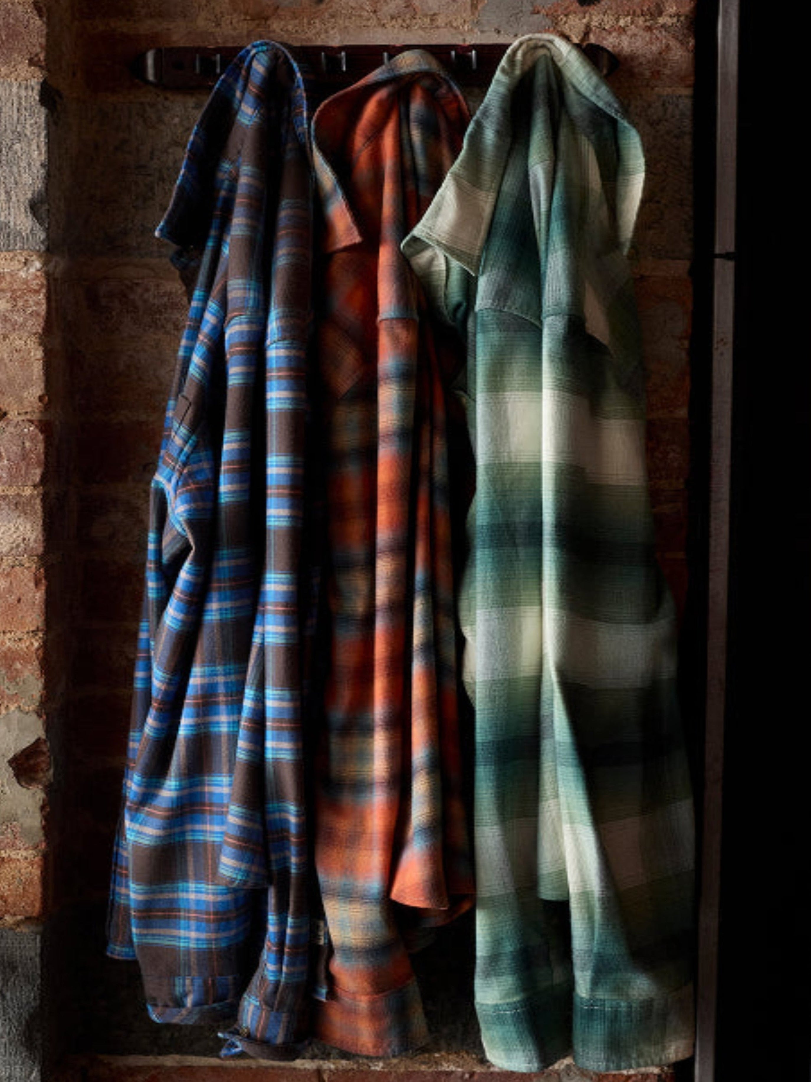 Three plaid shirts hanging on a rack against a brick wall.
