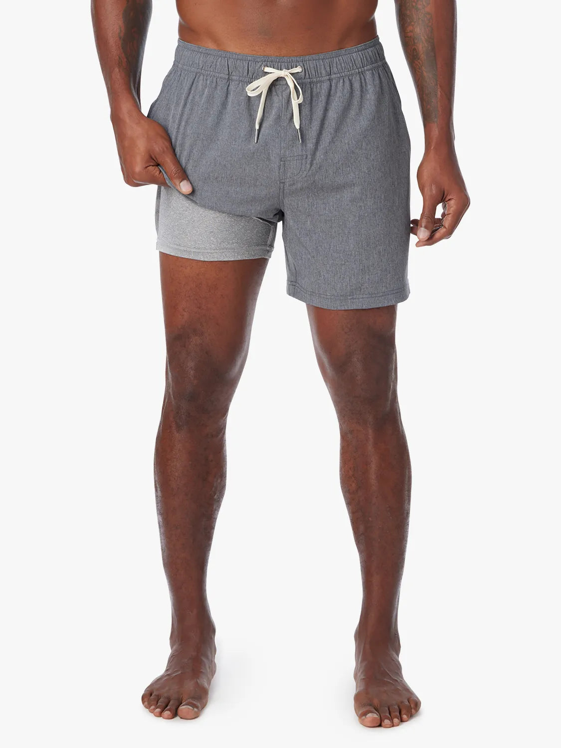 Man wearing a grey one shorts in 8 inch inseam with a drawstring on a white background, showing the liner underneath. 