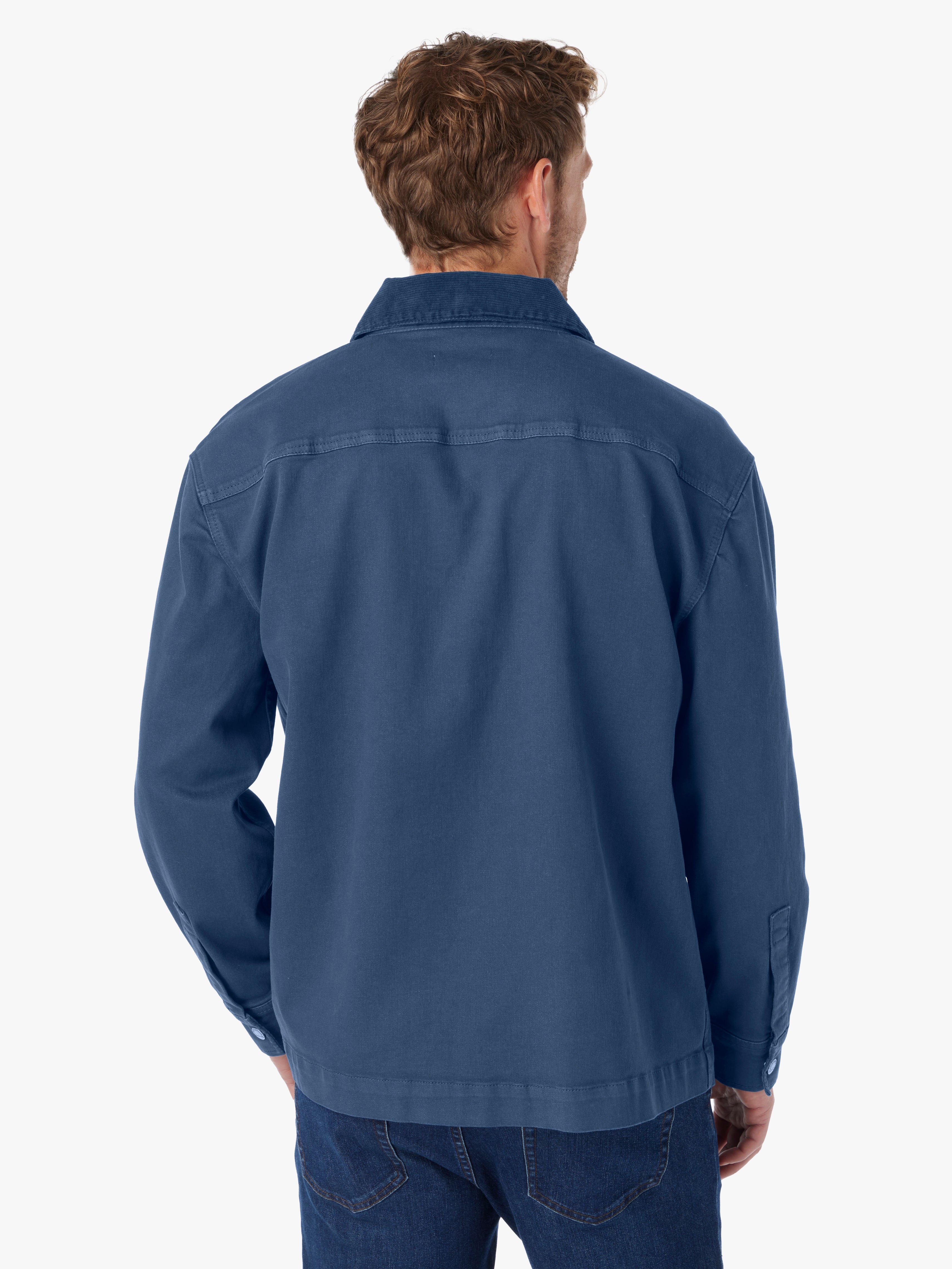 Man wearing blue barn style jacket with brown button details and tonal corduroy collar on a white background. Showing the back view of jacket. 