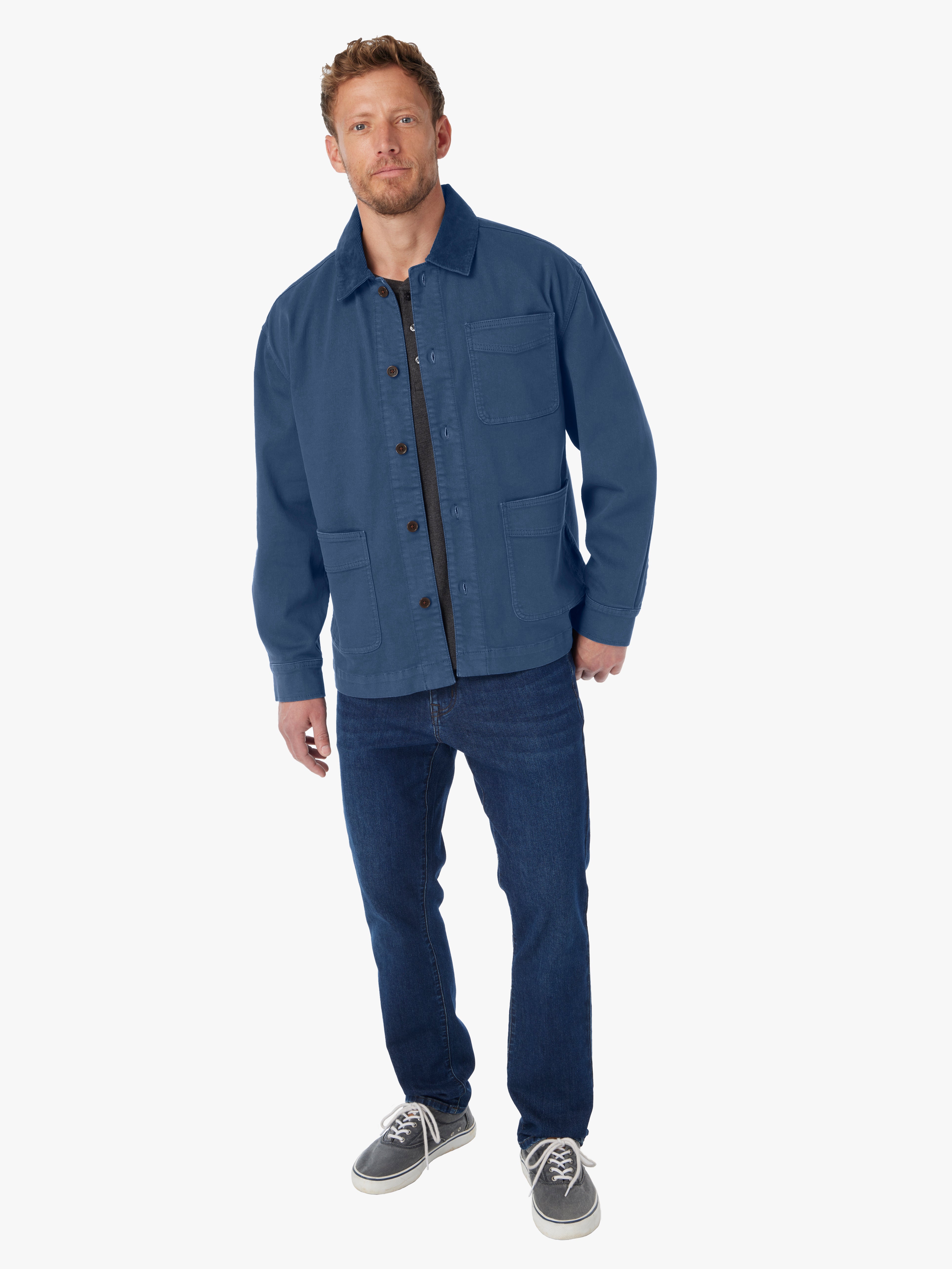 Man wearing blue barn style jacket with brown button details and tonal corduroy collar on a white background. 