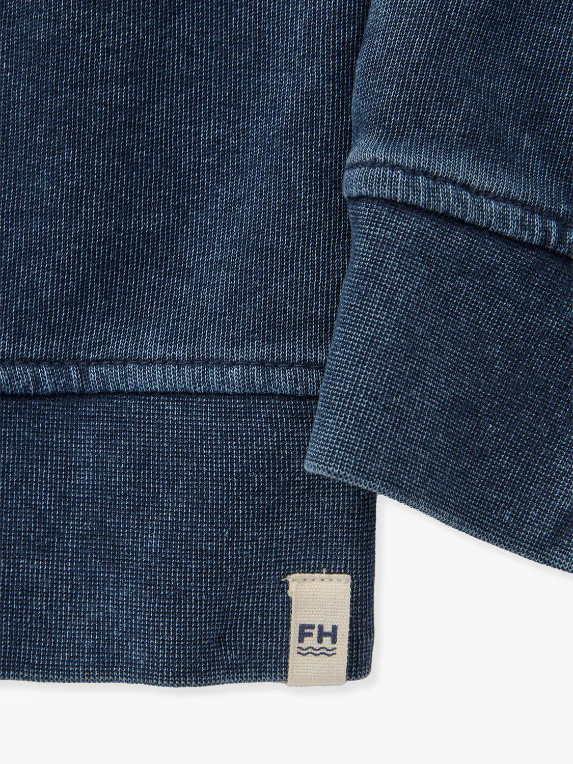 Close-up of a navy blue textured fabric for saltaire sweatshirt with a brand label on a white background