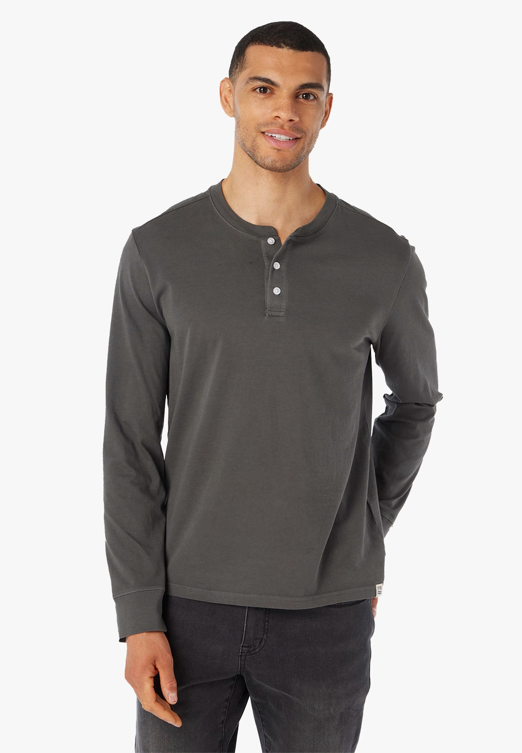 Man wearing a black long-sleeve henley shirt on a white background paired with black driftwood denim. 