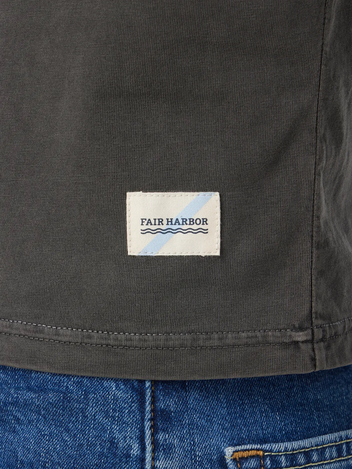 Close up of black saltaire t-shirt  fabric and brand logo patch paired with denim pants.