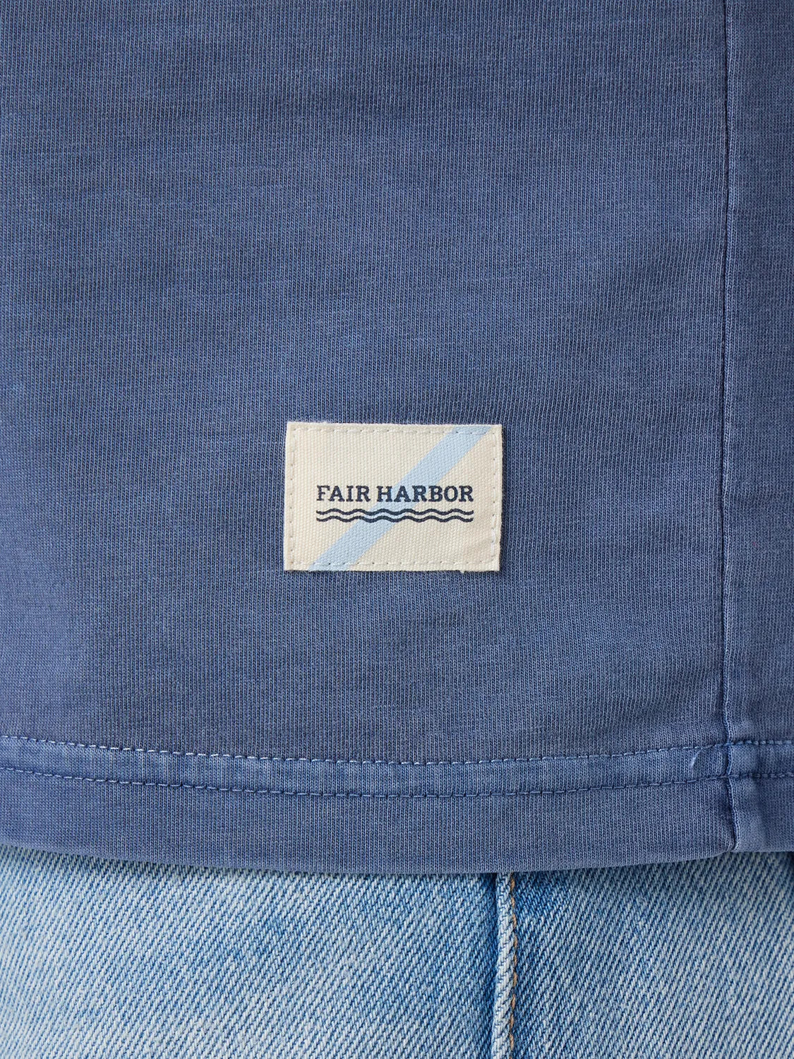 Close up of navy blue saltaire t-shirt fabric and brand logo patch at bottom hem. 