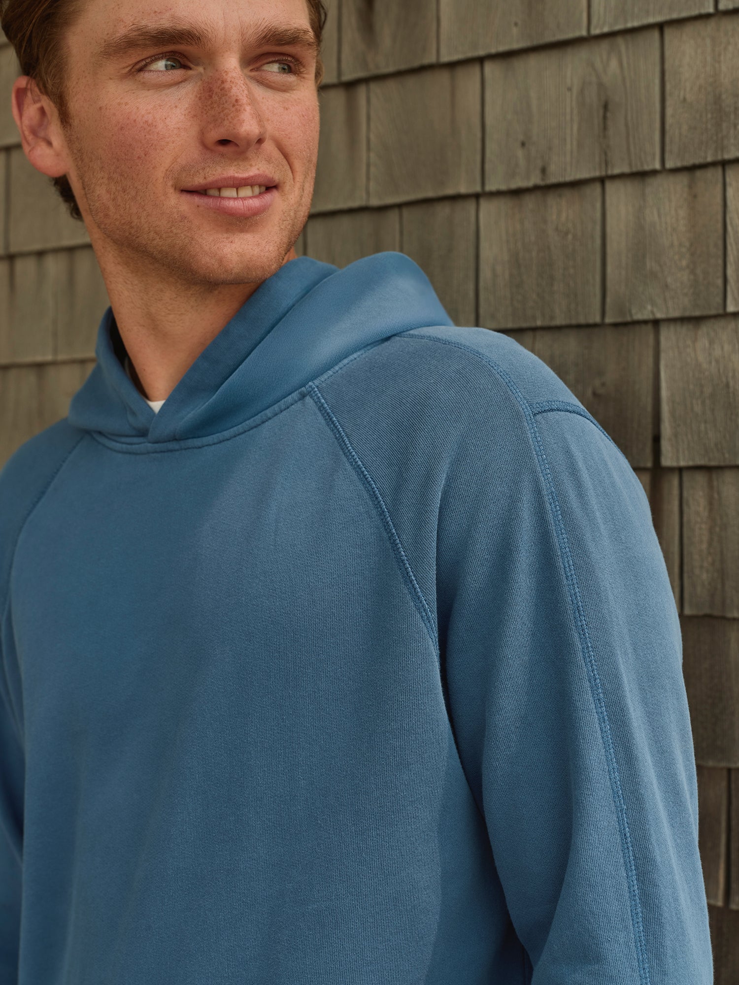 Man standing outside against wall wearing blue hoodie and looking away 