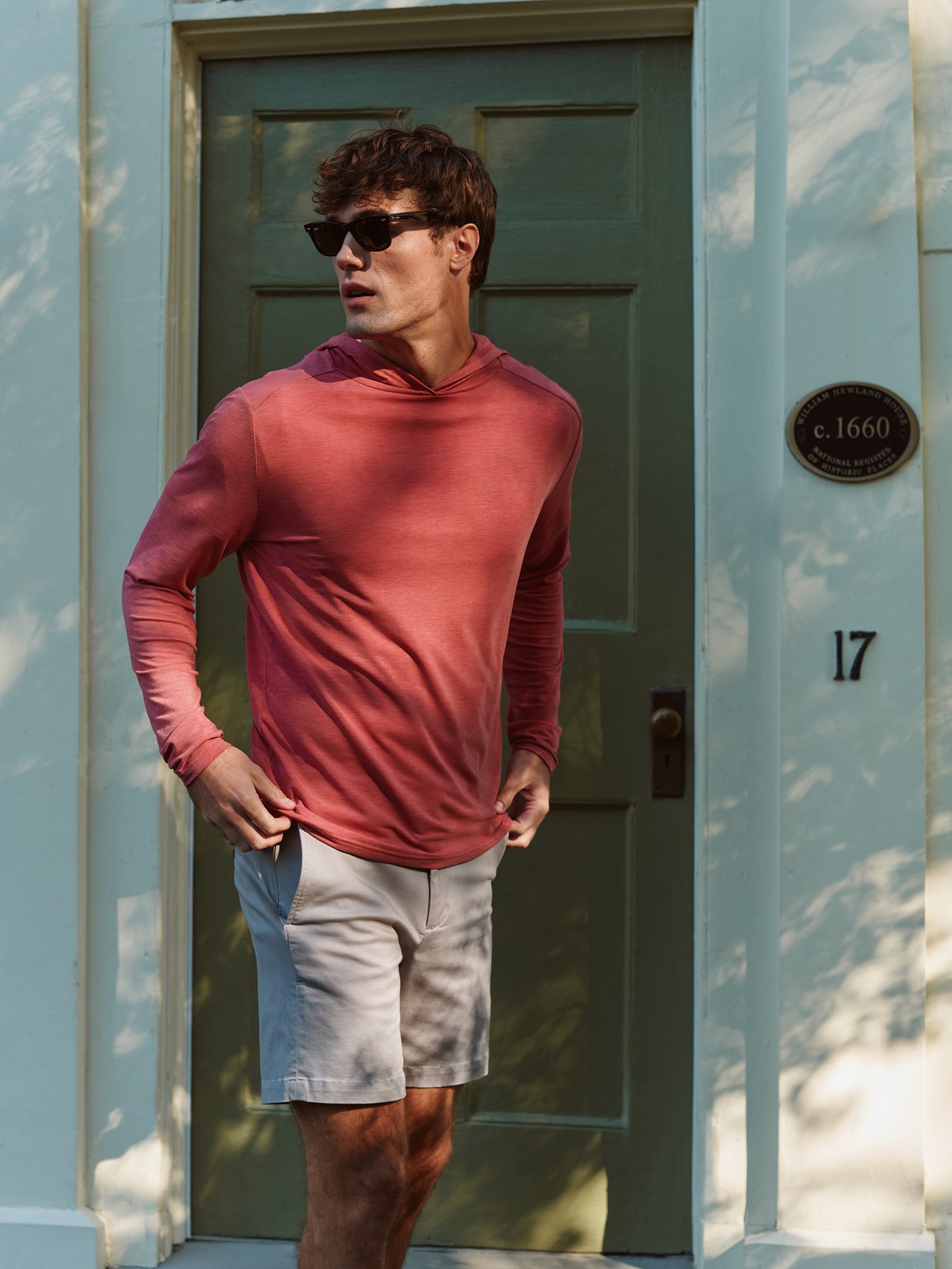 Man standing outside in front of a door wearing red Seabreeze hoodie with horizon short and sunglasses 