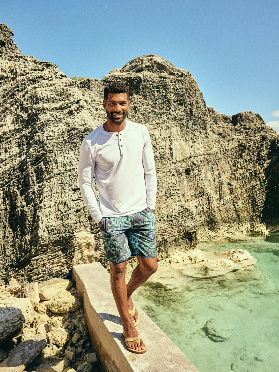 Man walking on along ocean wall wearing henley long sleeve tee and the anchor trunk 8 inch in navy evergreen pattern. 