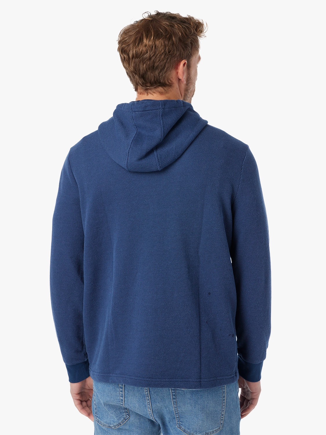Man wearing a navy blue hoodie and driftwood denim pants on a white background, showing the back view of hoodie. 