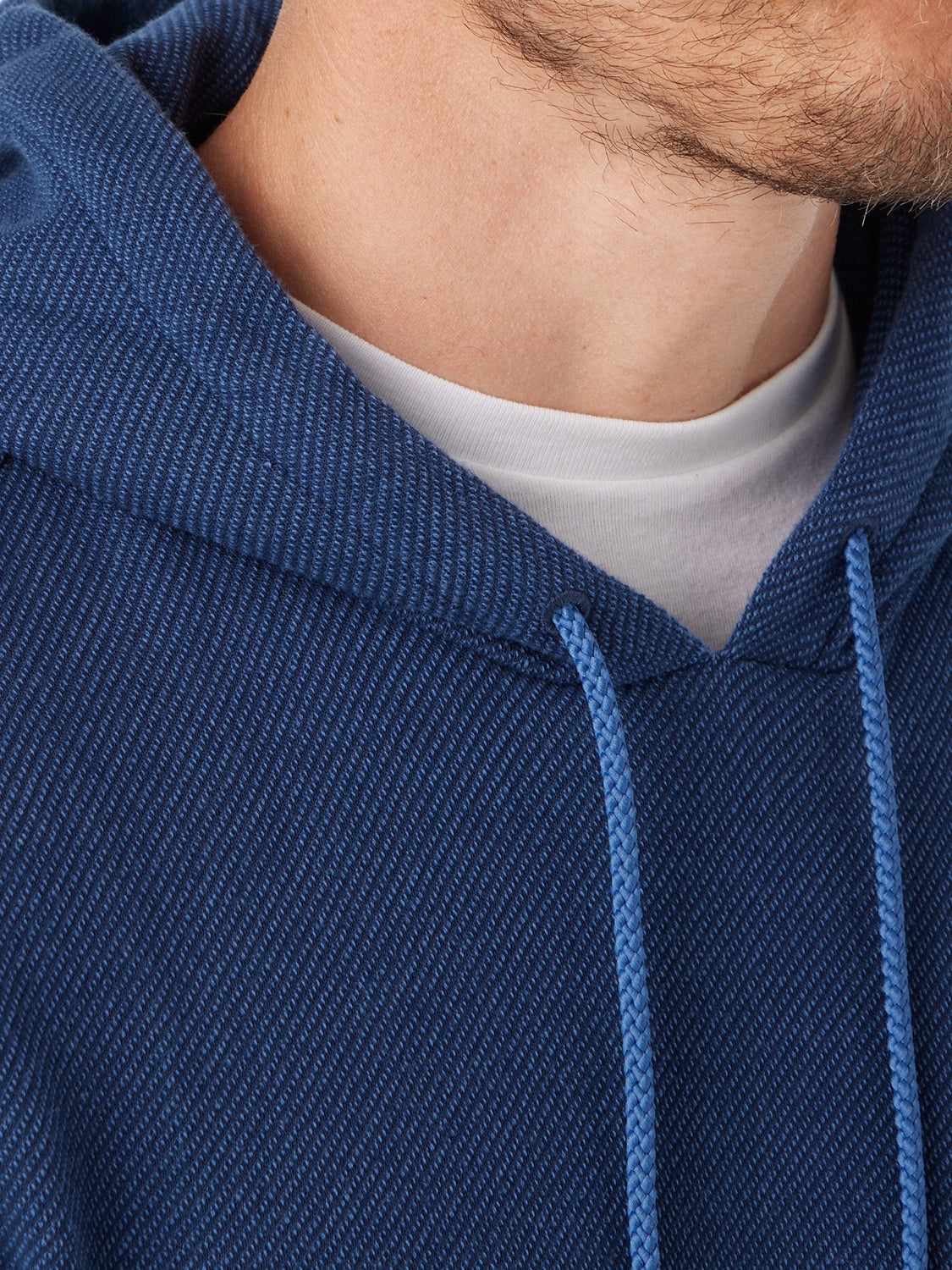 Close-up of a person wearing a navy blue hoodie with navy drawstring detail and  a white shirt underneath.
