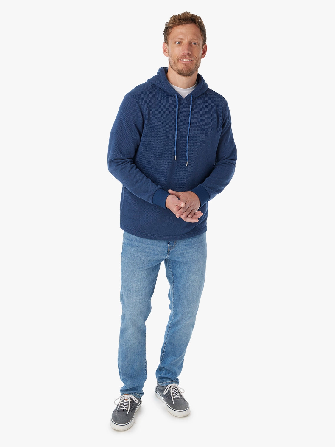 Man wearing a navy blue hoodie with navy drawstrings,  paired with white tshirt underneath hoodie and driftwood denim pants on a white background
