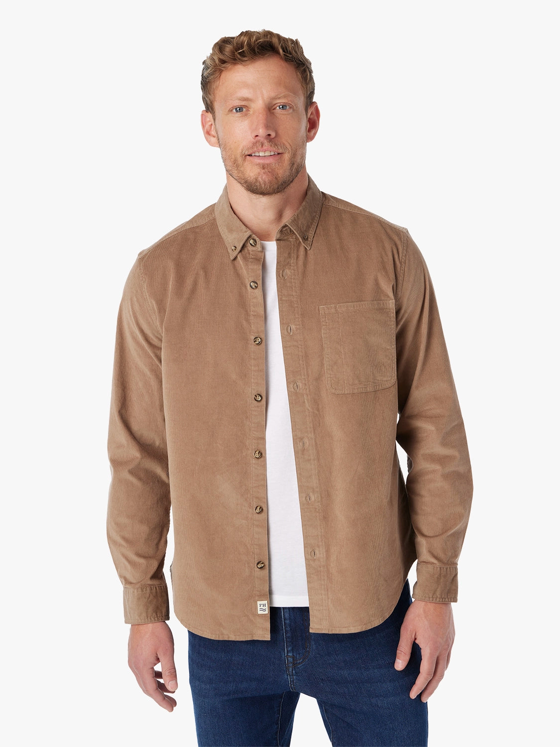 Man wearing a brown corduroy button-up shirt over a white t-shirt with a white background with pair of driftwood denim. 