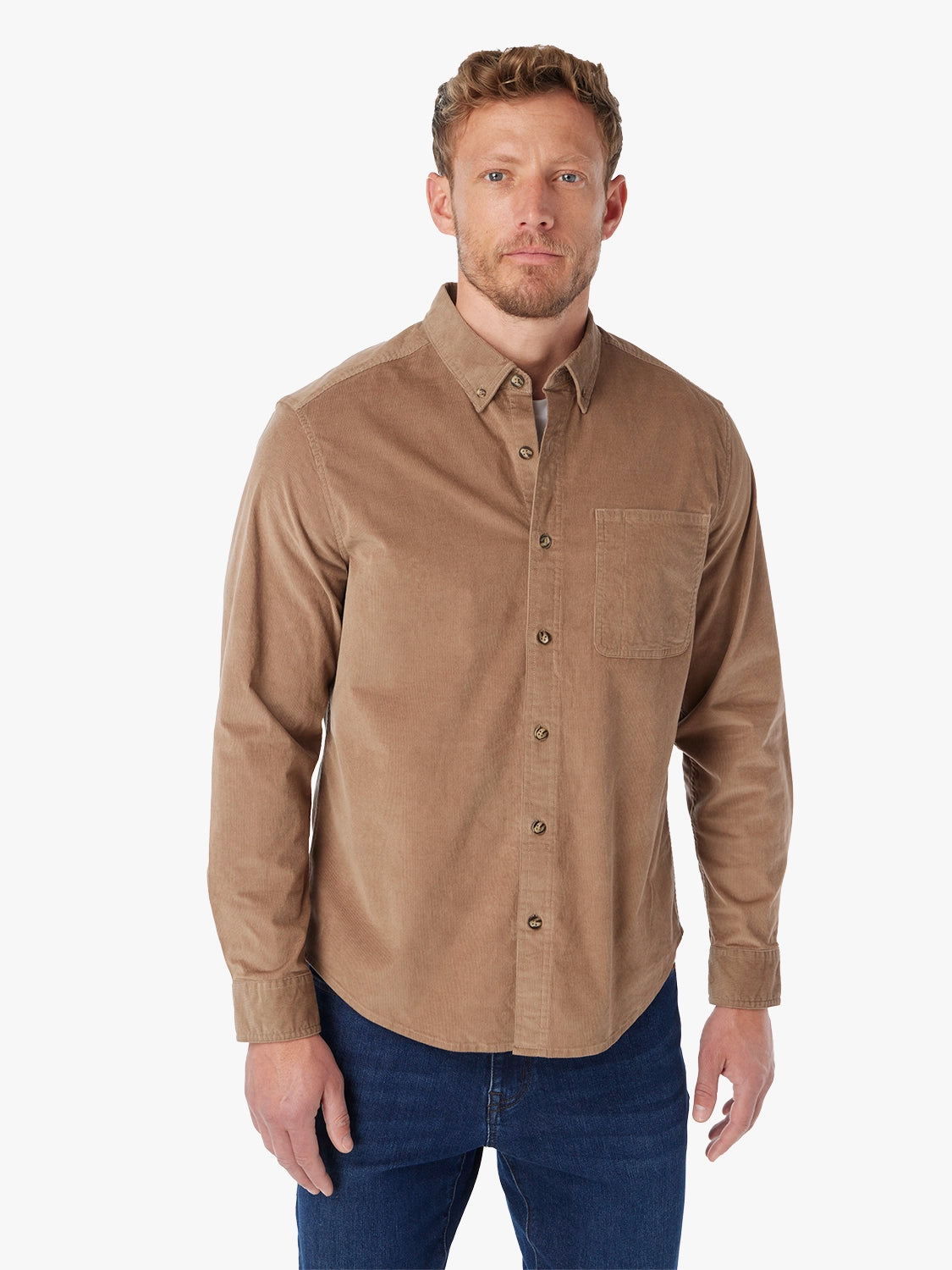 Man wearing a brown corduroy button-up shirt over a white t-shirt with a white background with pair of driftwood denim. 
