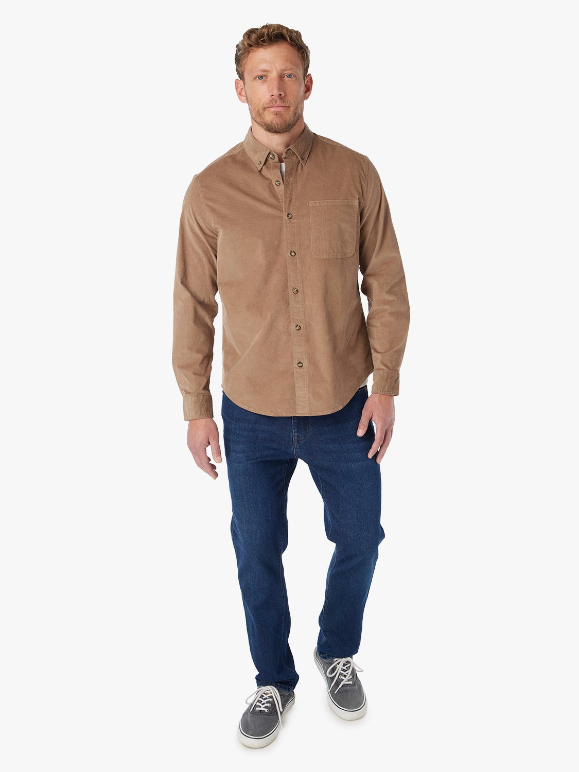 Man wearing a brown corduroy button-up shirt over a white t-shirt with a white background with pair of driftwood denim. 