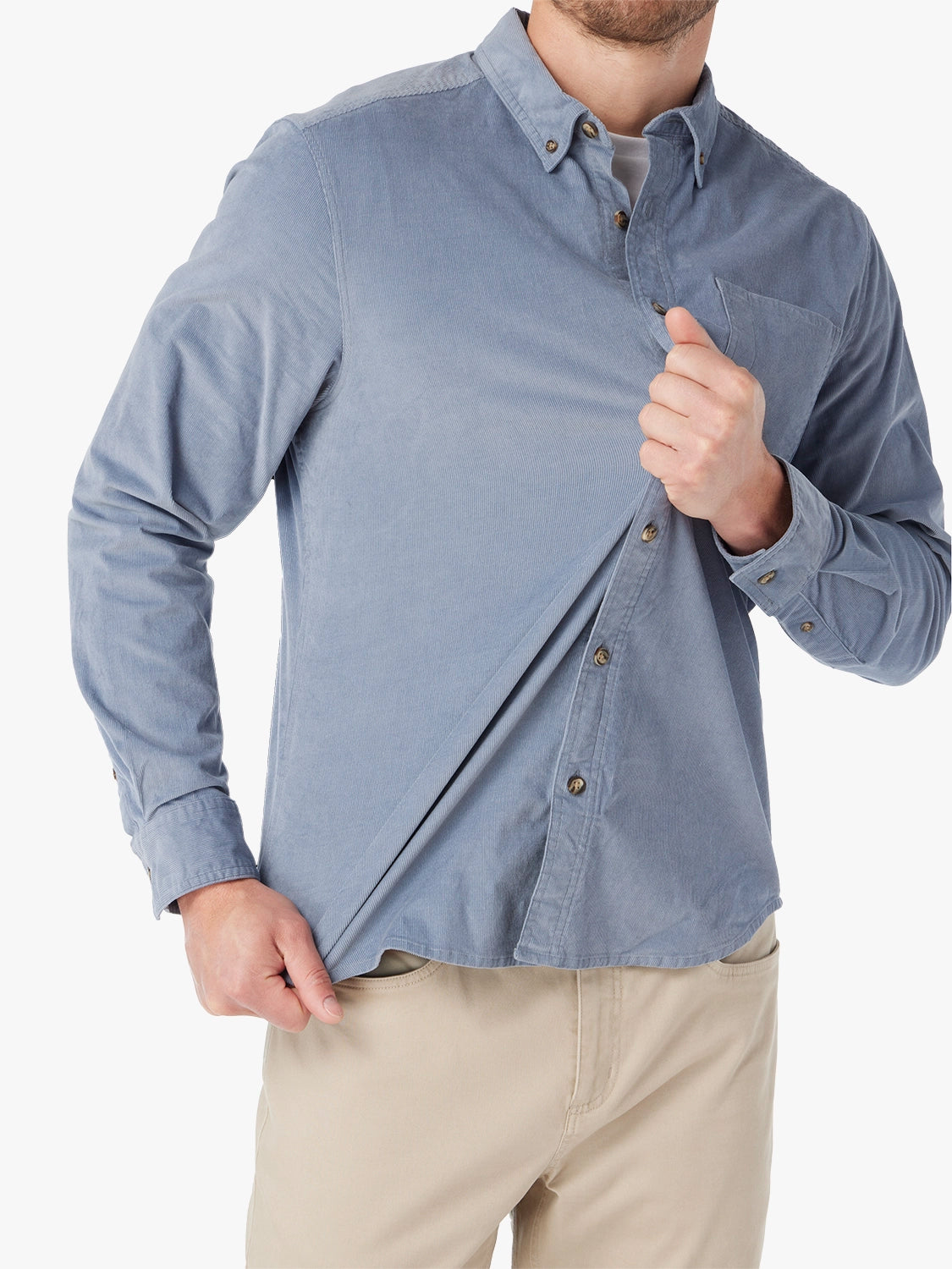 Man wearing blue corduroy button-up shirt on a white background. Paired with khaki horizon pants, pulling on the shirt with both hands to demonstrate the stretch ability of fabric. 