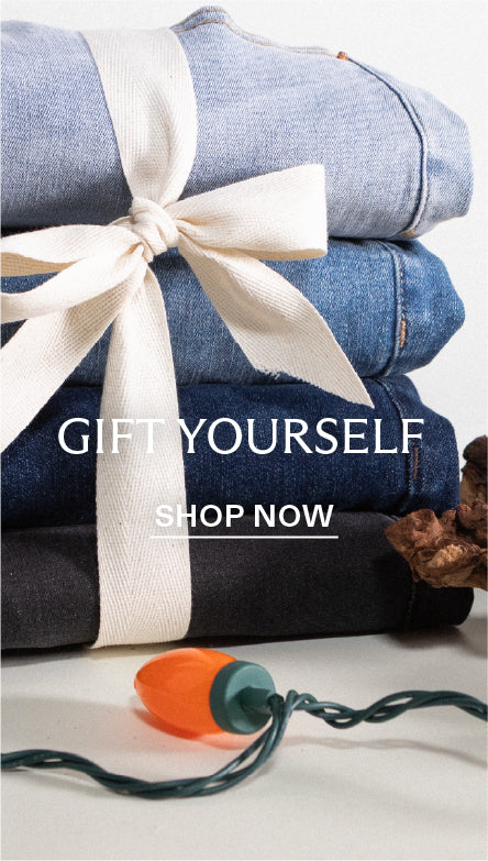 Stack of folded jeans with a white ribbon and bow, surrounded by Christmas decorations on a white background. With text overlay 